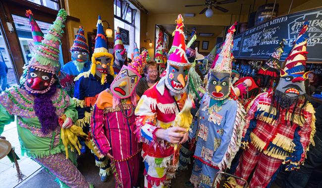 Mardi Gras troupe in colourful tasselled shirts and trousers, decorated masks and pointed hats.