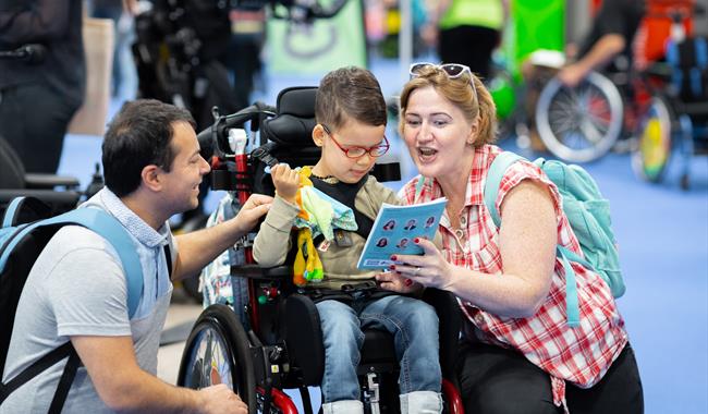 Image of a mum and dad with boy in a wheelchair, reading a book at an exhibition as a family.