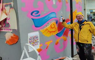 Artist Dave Pop creating a mural on a wall with spray paint.