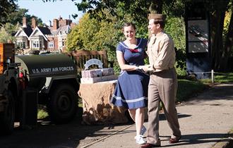 A couple jive dance outside at Bletchley Park. The Bletchley Park Mansion is in view behind them.