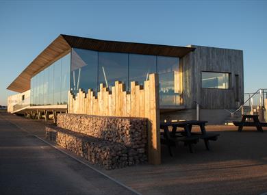 a photograph of Rye Harbour visitor centre. Wooden and glass structure against a blue sky.