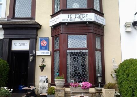 Front of a bed and breakfast called Le Maitre, with bay window and pink flowers in a windowbox