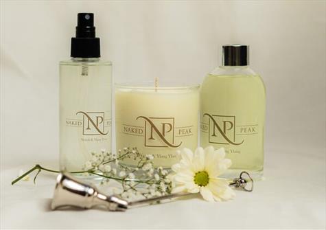 two clear bottles filled with pale yellow liquid, and candle. All branded with Naked Peak logo. Candle snuffer and gypsophilia in the foreground