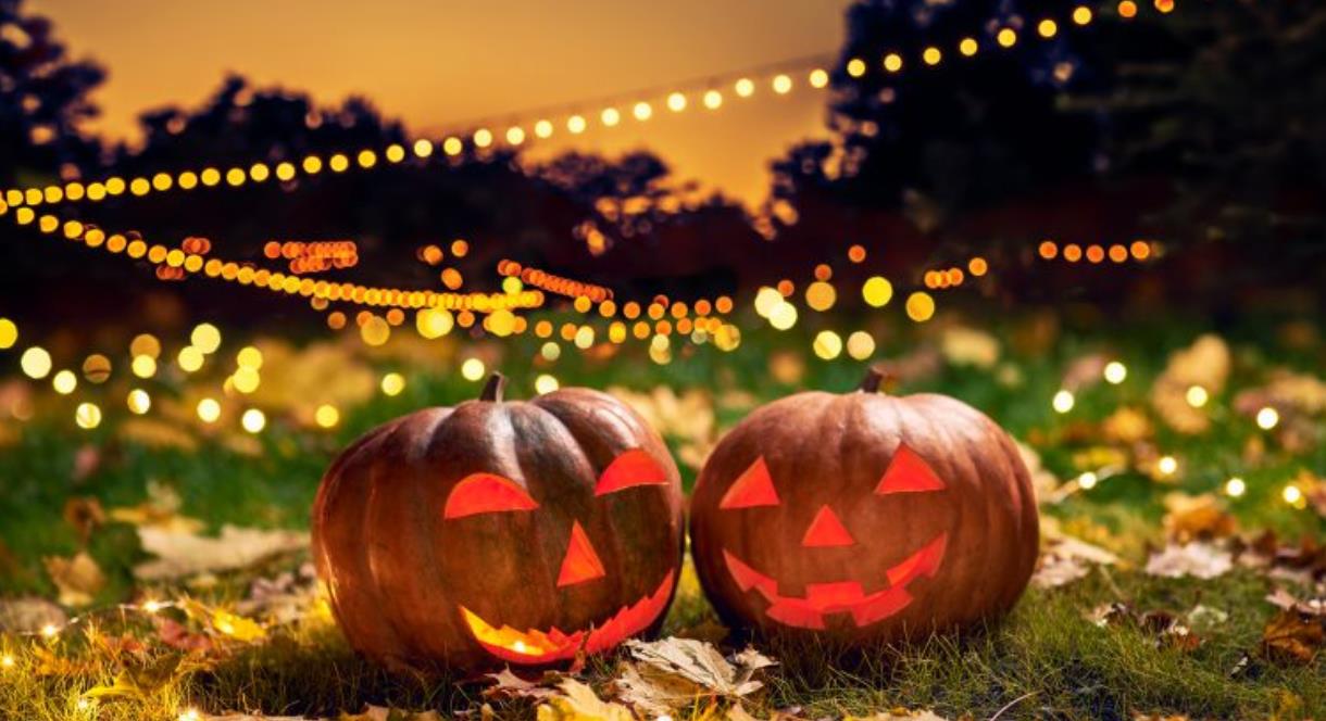 Two spooky carved pumpkins on the ground, surrounded by Autumn leaves and lighting