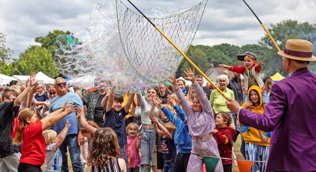 A man with a huge net creates hundreds of bubbles in front of a crowd of people, mostly children