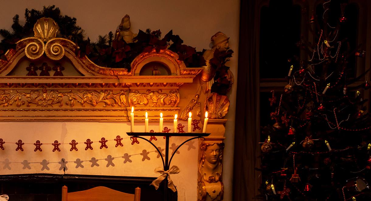 Candles on a candelabra beside a Christmassy-looking fireplace