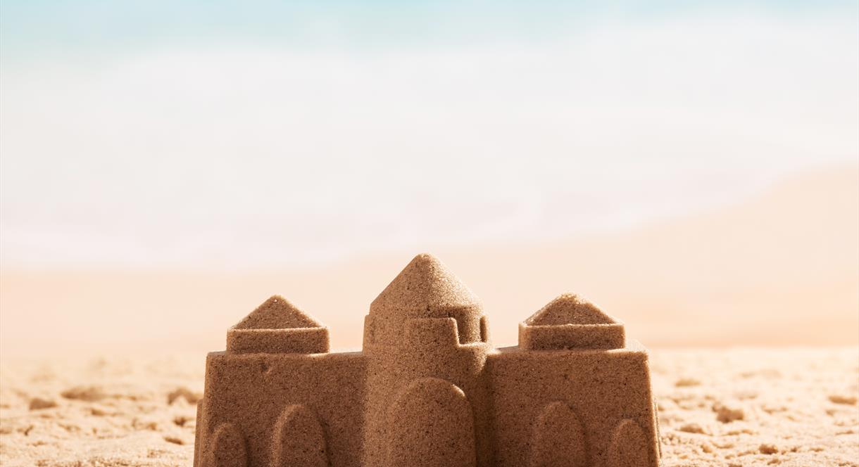 Image shows a sandcastle on a beach