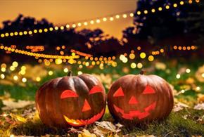 Two spooky carved pumpkins on the ground, surrounded by Autumn leaves and lighting