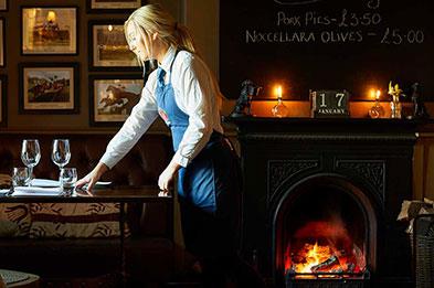 Waitress serving table near real log fire