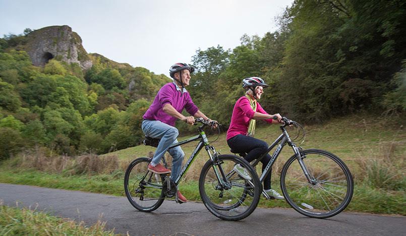 Couple cycling on the Manifold Track with Thor's Cave in the background, Manifold Valley, Peak District, Staffordshire.