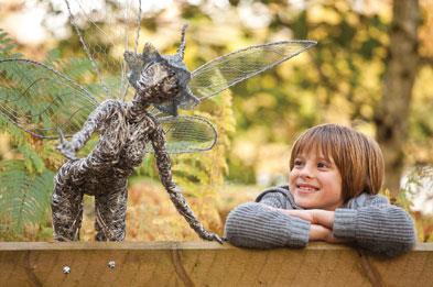 Boy leaning on gate admiring fairy sculpture in Trentham Gardens
