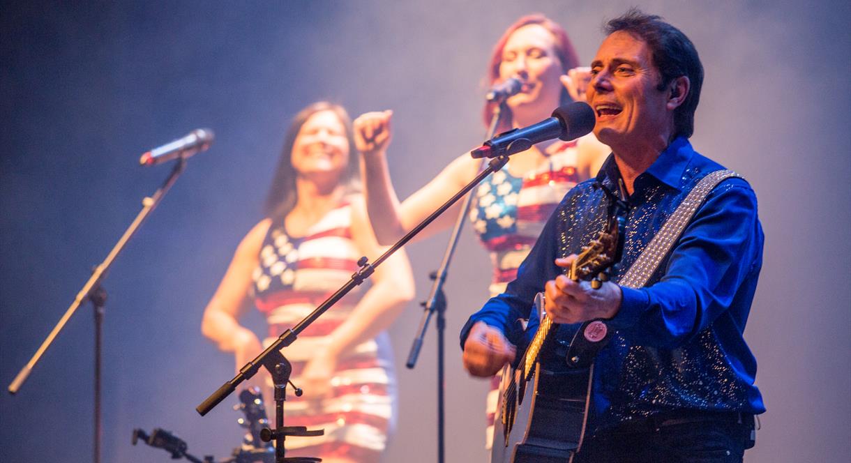 Image shows a Neil Diamond tribute performing on stage with his backing singers