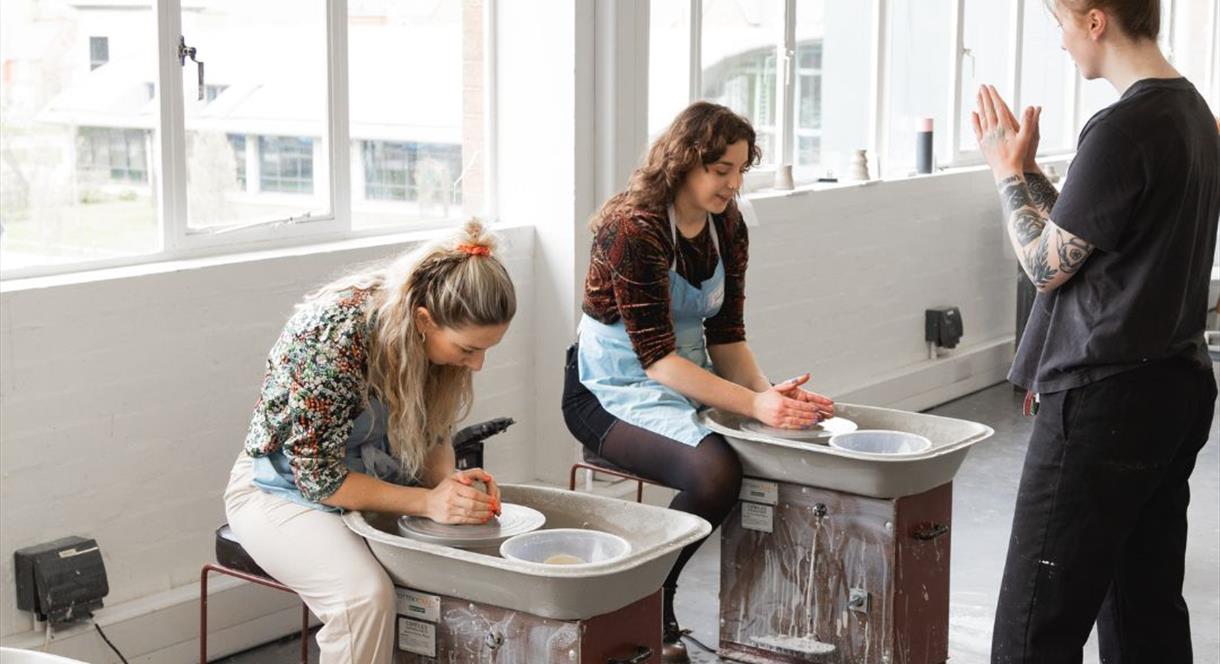 Image shows two women try their hand at pottery in the decorating studio at World of Wedgwood