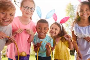 A group of children with Easter eggs in baskets, wearing bunny ears, smile at the camera