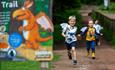 Image shows three boys, wearing dragon wings, running along The Zog Trail at Cannock Chase Forest