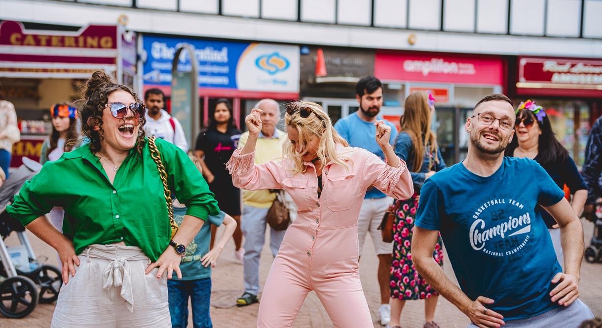 A group of performers dance in a busy shopping area