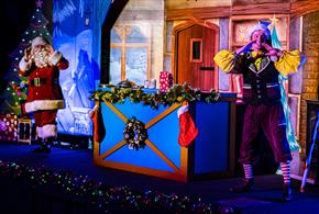 Image shows Santa and an elf performing on stage in front of a festive backdrop