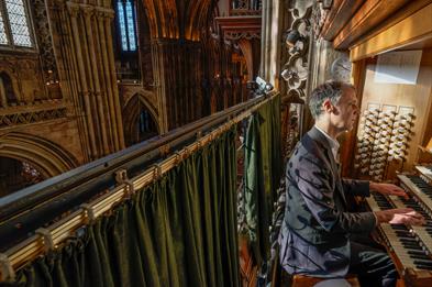 Image shows a man, on the right, playing the organ in a historic building, Lichfield Cathedral