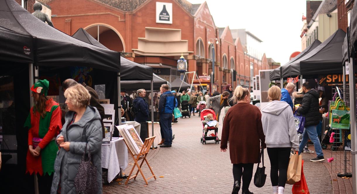 Image shows stalls and shoppers at the Potteries Artisan Market on a grey day