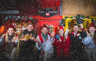 Image shows some of the performers from North Pole Adventure, in costumes, as snow falls down