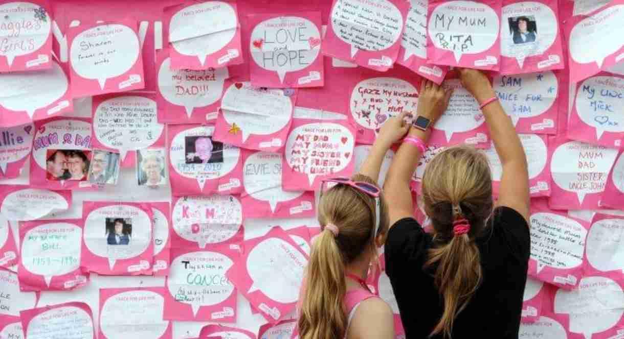 Image shows two women reading the messages on the board at a Race for Life event
