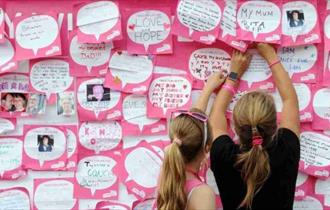 Image shows two women reading the messages on the board at a Race for Life event