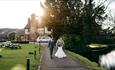 Image shows a couple walking down the path after their wedding, as the sun begins to set behind the farm house