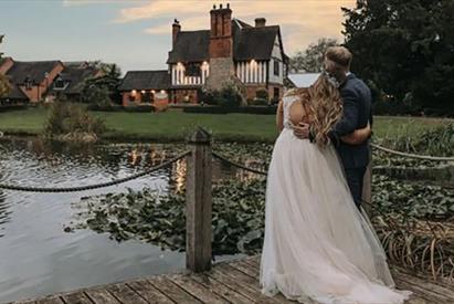 Image shows a bride and groom, at dusk, looking over the lake at the farm house on their big day