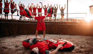 A group of people dressed in Roman attire standing around a battle arena cheering two people in the middle.