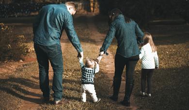 Young family walking a green forest and holding hands with their toddler