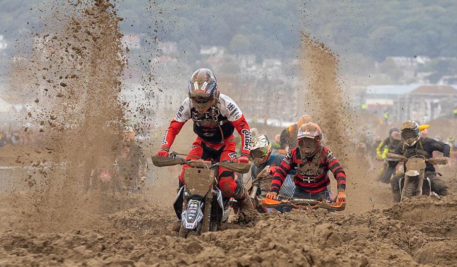 Sand flies up as three motorbike riders struggle through sand in a beach race