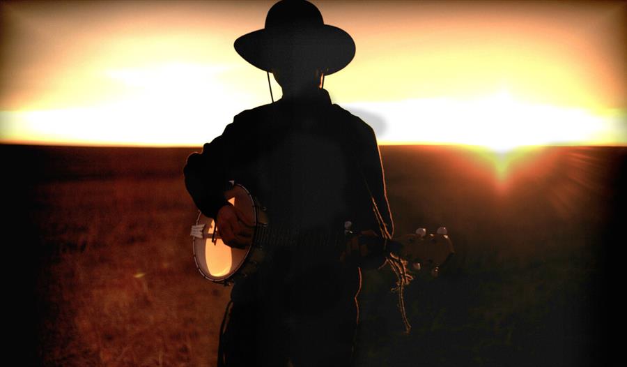 Silhouette of a person wearing a cowboy hat and playing a banjo