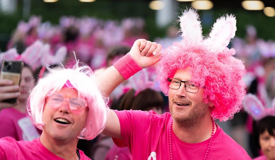 Two men in pink wigs and t-shirts smiling