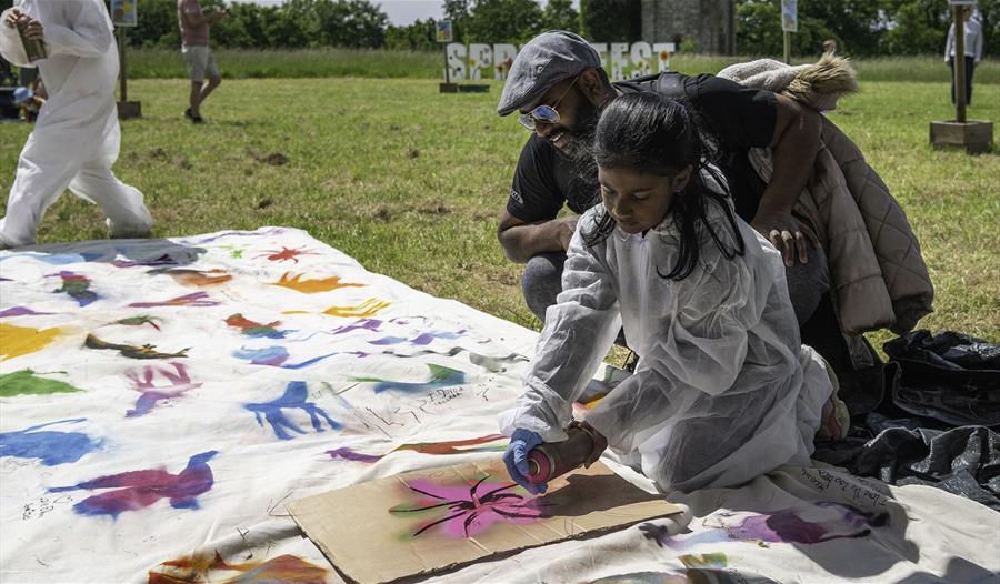 A parent and child spray paint colourful shapes on a cloth together