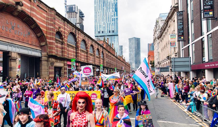 Colourful Manchester Pride Parade with people watchihng and cityscape in the background