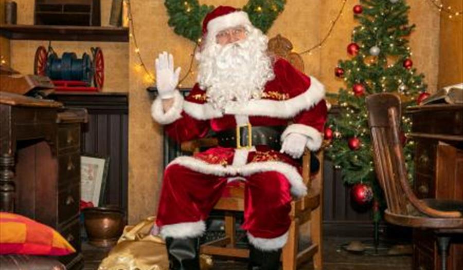 santa sat on a chair with a decorated christmas tree in the background