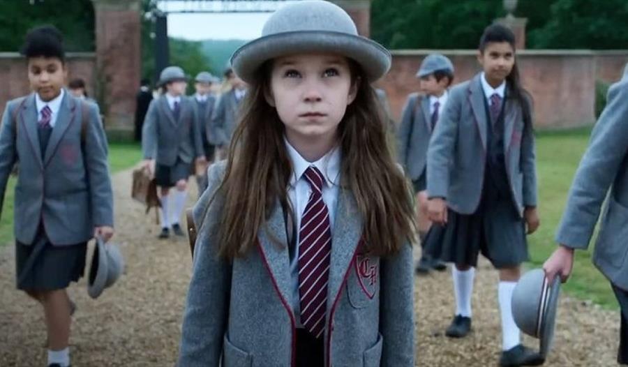 Matilda in a grey hat and school uniform walking through school gates with other children