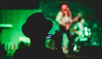 Person recording video of a person playing guitar onstage