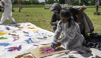 A parent and child spray paint colourful shapes on a cloth together