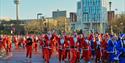 A group of runners dressed as santa in red and blue suits on The Strand waving at the camera.