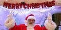 Santa is pointing to a sign that reads 'Merry Christmas!'