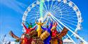 5 men playing instruments whilst dressed in colourful clothing in front of Bournemouths big wheel