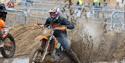 A motorcyclist kicks up a lot of muck and water behind him as his bike is stuck deep in a puddle during a bike race on a beach