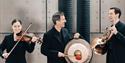 Three musicians, one with a violin, one with a tuba, and the other with what looks like a cymbal
