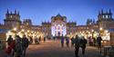 People walk amongst brightly lit chalets in front of Blenheim Palace