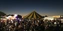 Photo of a crowd at riverside festival, in groups sat on benches and enjoying the stalls.