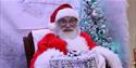 Santa is looking at the camera and offering a present