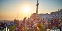 Crowds on Plymouth Hoe at sunset, with fairground rides in the background