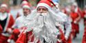 Man dressed up in a red santa costume with a long white beard running.