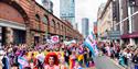 Colourful Manchester Pride Parade with people watchihng and cityscape in the background